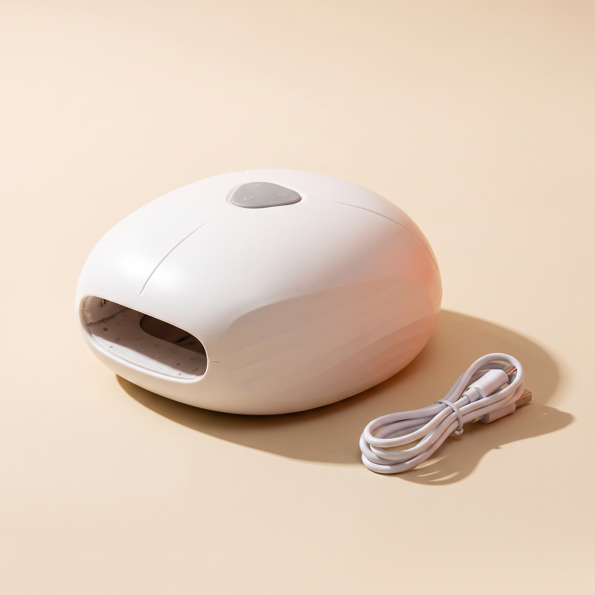 White hand massage device with charging cable on a cream studio backdrop